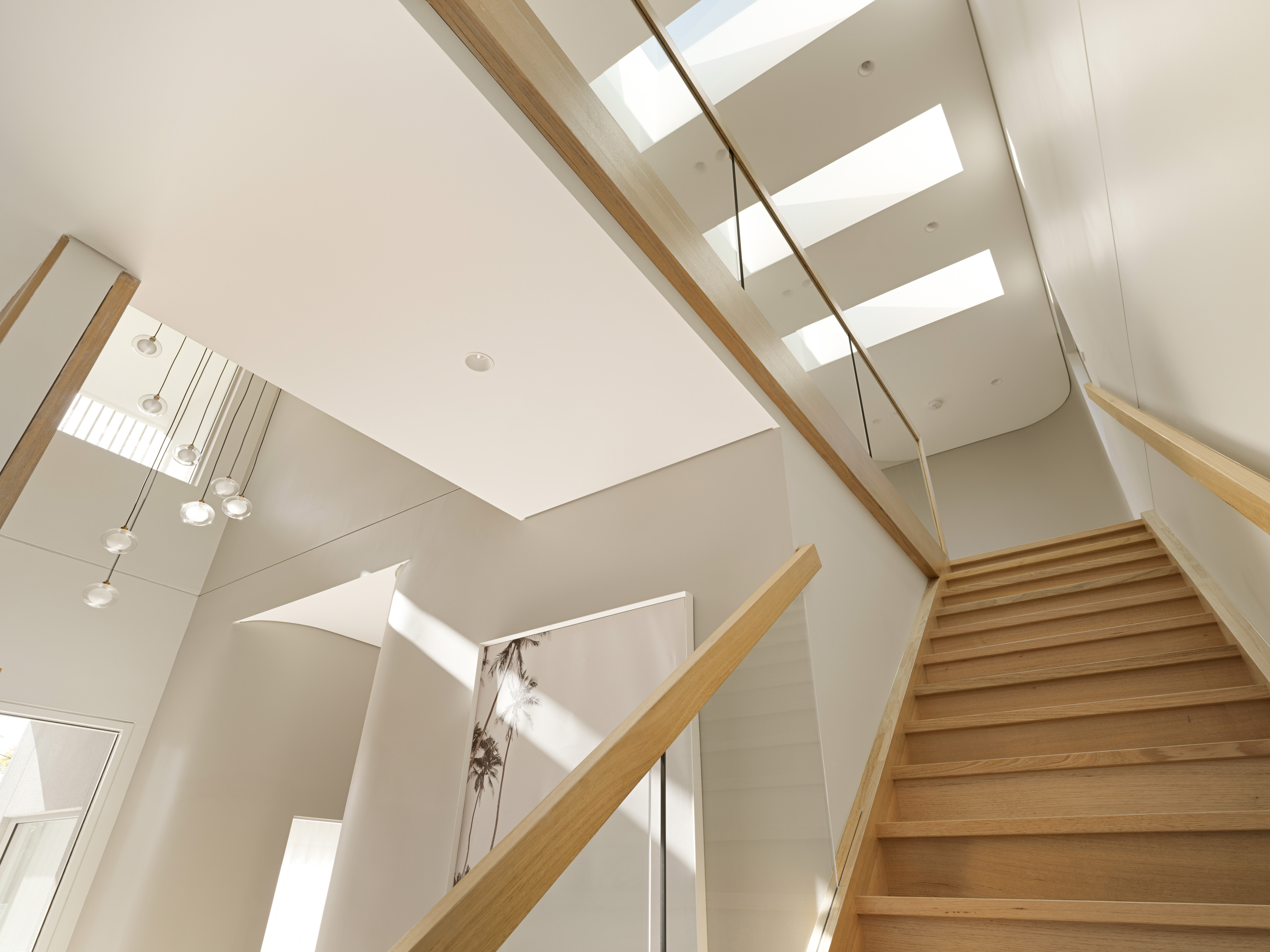 Modern staircase with wooden steps and glass railing, illuminated by natural light from skylights above.